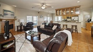 A spacious living room with a fireplace, leather sofas, a coffee table, and a kitchen area with cabinets and a countertop. - Casa de la Perla, Ocean Views & Beach Boardwalk (Port Aransas)