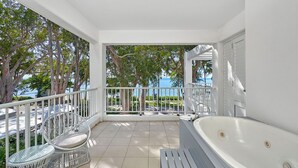 A balcony with a white bathtub, wicker chairs, and a view of the sea. - Beach Club Top Floor Oceanfront Studio Palm Cove (Palm Cove)
