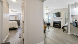 A modern living room with a fireplace, a television mounted on the wall, and a ceiling fan. - The Gray Retreat - Luxury Condo (Fayetteville)