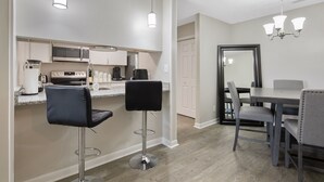 A modern kitchen with stainless steel appliances, a bar area with two stools, and a dining table with four chairs. - The Gray Retreat - Luxury Condo (Fayetteville)