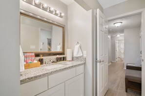 A bathroom with a vanity, mirror, towel rack, and a door leading to another room. - The Gray Retreat - Luxury Condo (Fayetteville)