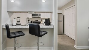 A modern kitchen with two bar stools, a microwave, a coffee maker, and a refrigerator. - The Gray Retreat - Luxury Condo (Fayetteville)