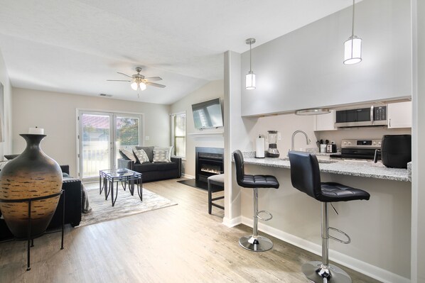 A modern kitchen with a bar area, a fireplace, and a dining area with a large vase. - The Gray Retreat - Luxury Condo (Fayetteville)