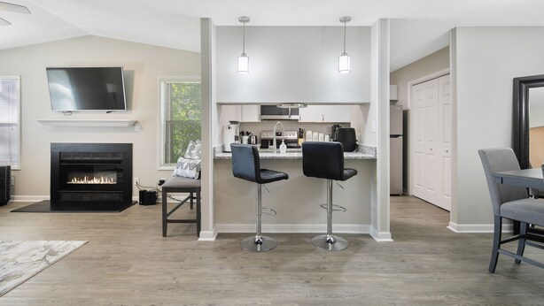 A modern living room with a fireplace, a TV mounted on the wall, and two bar stools. - The Gray Retreat - Luxury Condo (Fayetteville)