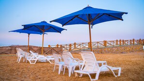 Beach chairs and umbrellas arranged on the sand, with a wooden fence in the background. - Marina Wadi Degla Hotel (Ataqah)