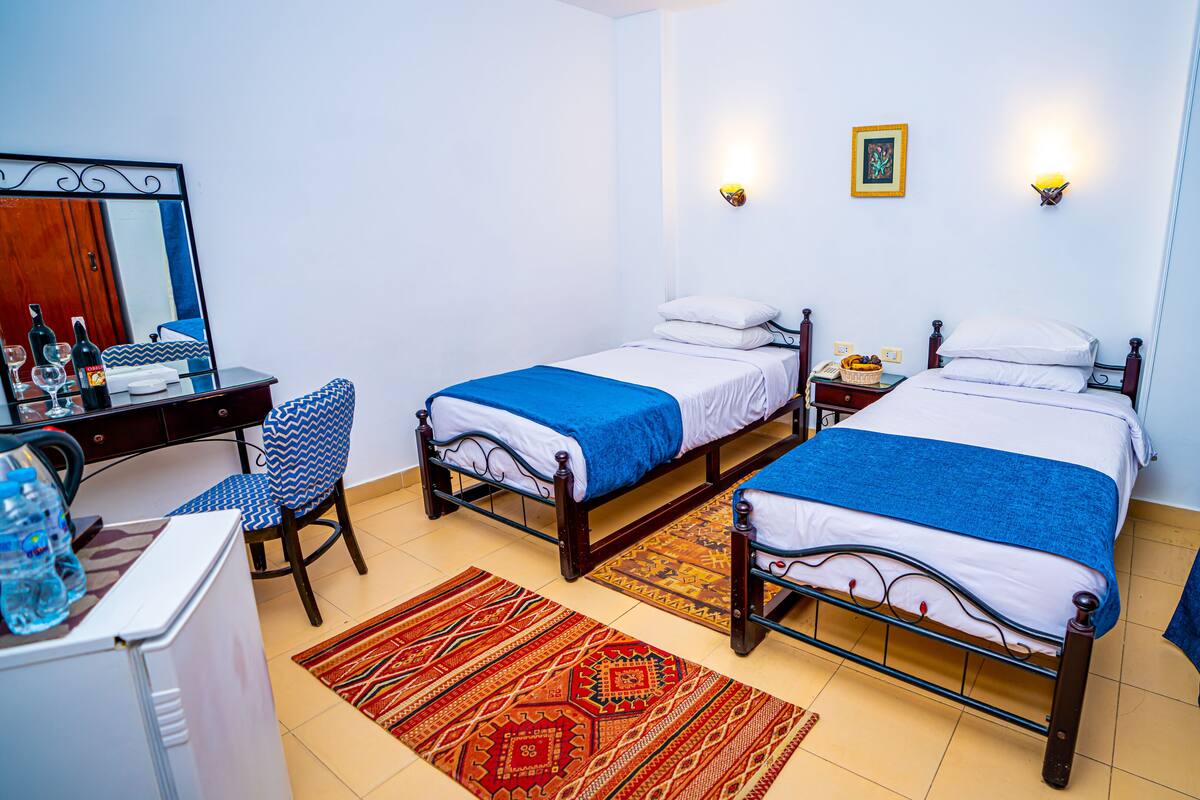 Een hotelkamer met twee bedden, een bureau met stoel, een spiegel en een klein tafeltje met lamp.
