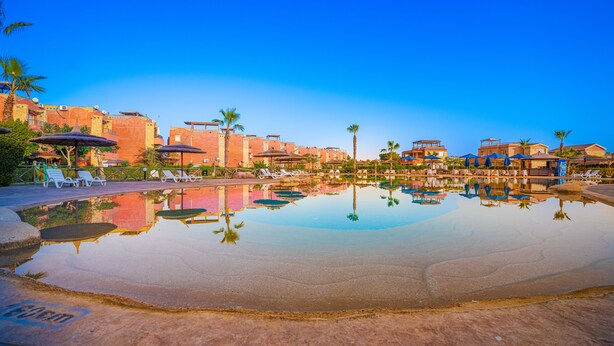 A clear pool with lounge chairs and umbrellas, surrounded by buildings with a Mediterranean architectural style. - Marina Wadi Degla Hotel (Ataqah)