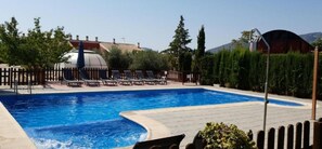 Una piscina con sillas de descanso y una pérgola, rodeada de vegetación y un paisaje de montañas.
