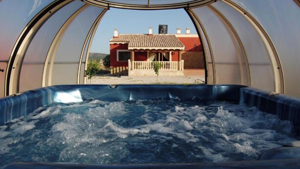 Banyera d'hidromassatge en una estructura transparent de cúpula amb vista a una casa vermella a l'exterior.