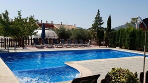 A swimming pool with lounge chairs and a fence, surrounded by trees and buildings. - 4 bedroom house (Caravaca de la Cruz)
