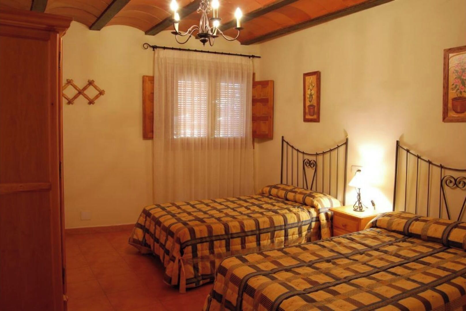 A bedroom with two beds, a chandelier, and a window with curtains.