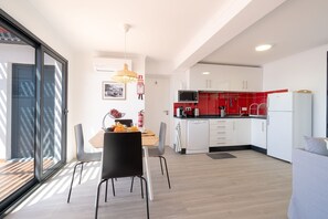 A modern kitchen with white cabinets, a red backsplash, and a microwave. There is a dining area with a table and chairs, and a sofa in the living area.