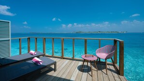 A wooden deck with a view of the ocean, a lounge chair, a pink chair, and a small table. - OBLU SELECT Lobigili  with Free Transfers (Lobigili)