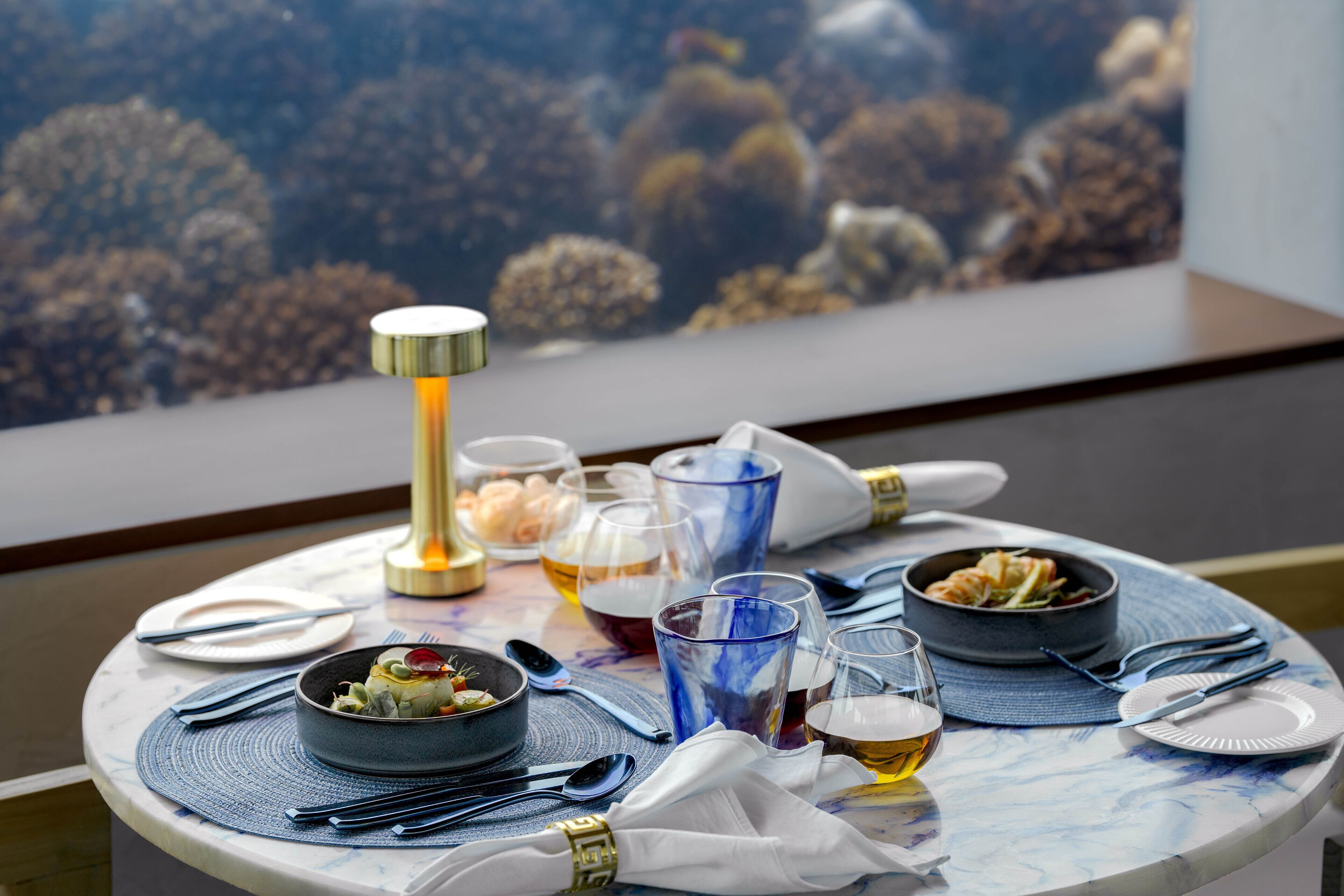 A dining table with various dishes, glasses, and cutlery, set on a marble table with a blue placemat.