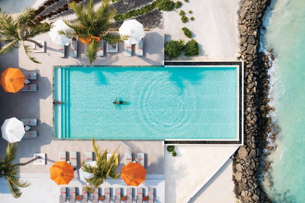 An aerial view of a rectangular swimming pool with lounge chairs and umbrellas, surrounded by a rocky shoreline and palm trees. - OBLU SELECT Lobigili  with Free Transfers (Lobigili)