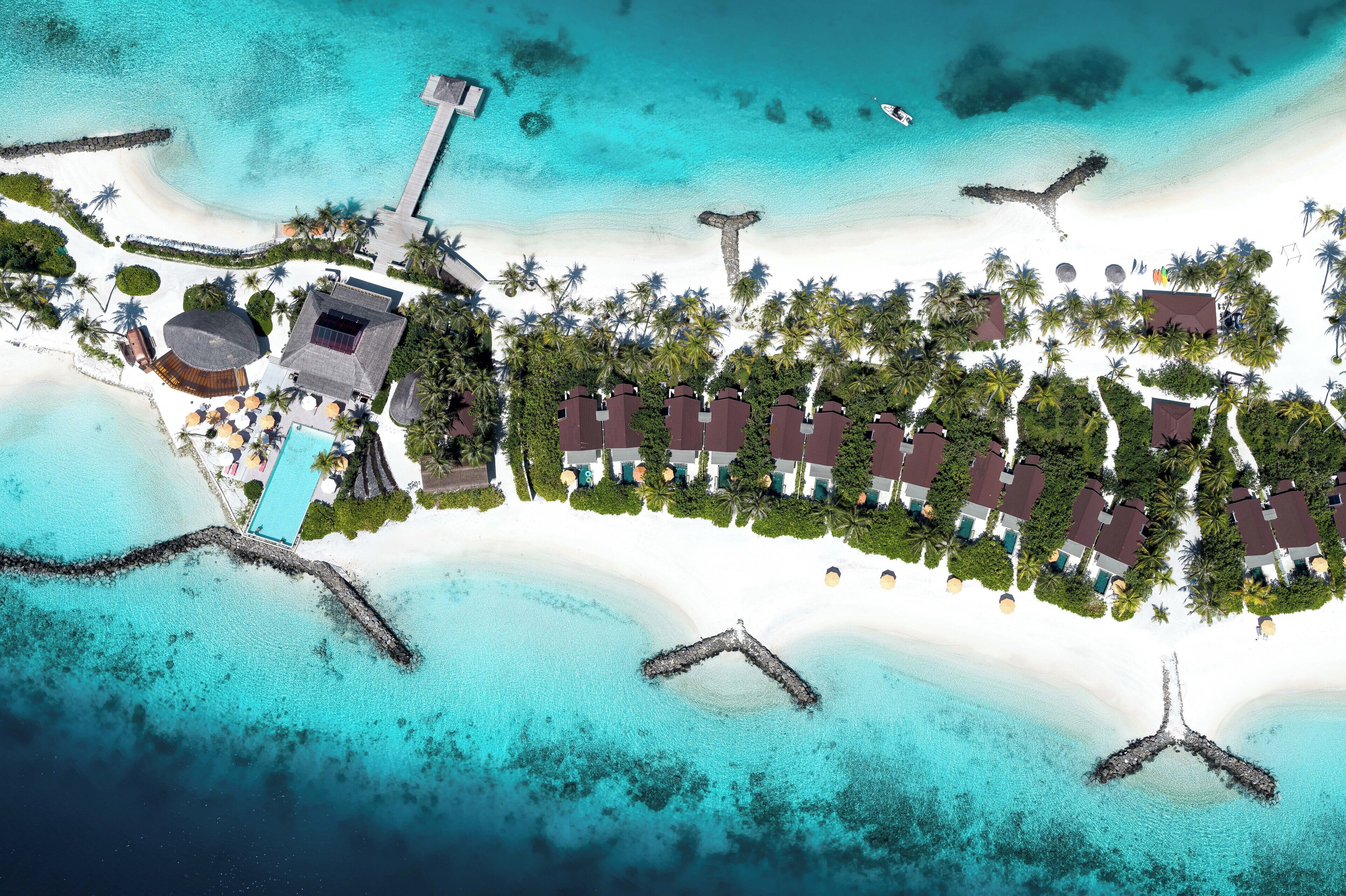 An aerial view of a resort with multiple bungalow-style buildings, a central pool, and surrounding palm trees.