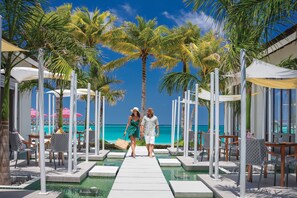 A couple walking on a poolside pathway with palm trees and umbrellas, overlooking a clear blue sea. - OBLU SELECT Lobigili  with Free Transfers (Lobigili)