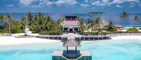 An overwater bungalows with a thatched roof, a pool, and a view of the ocean and a distant island.