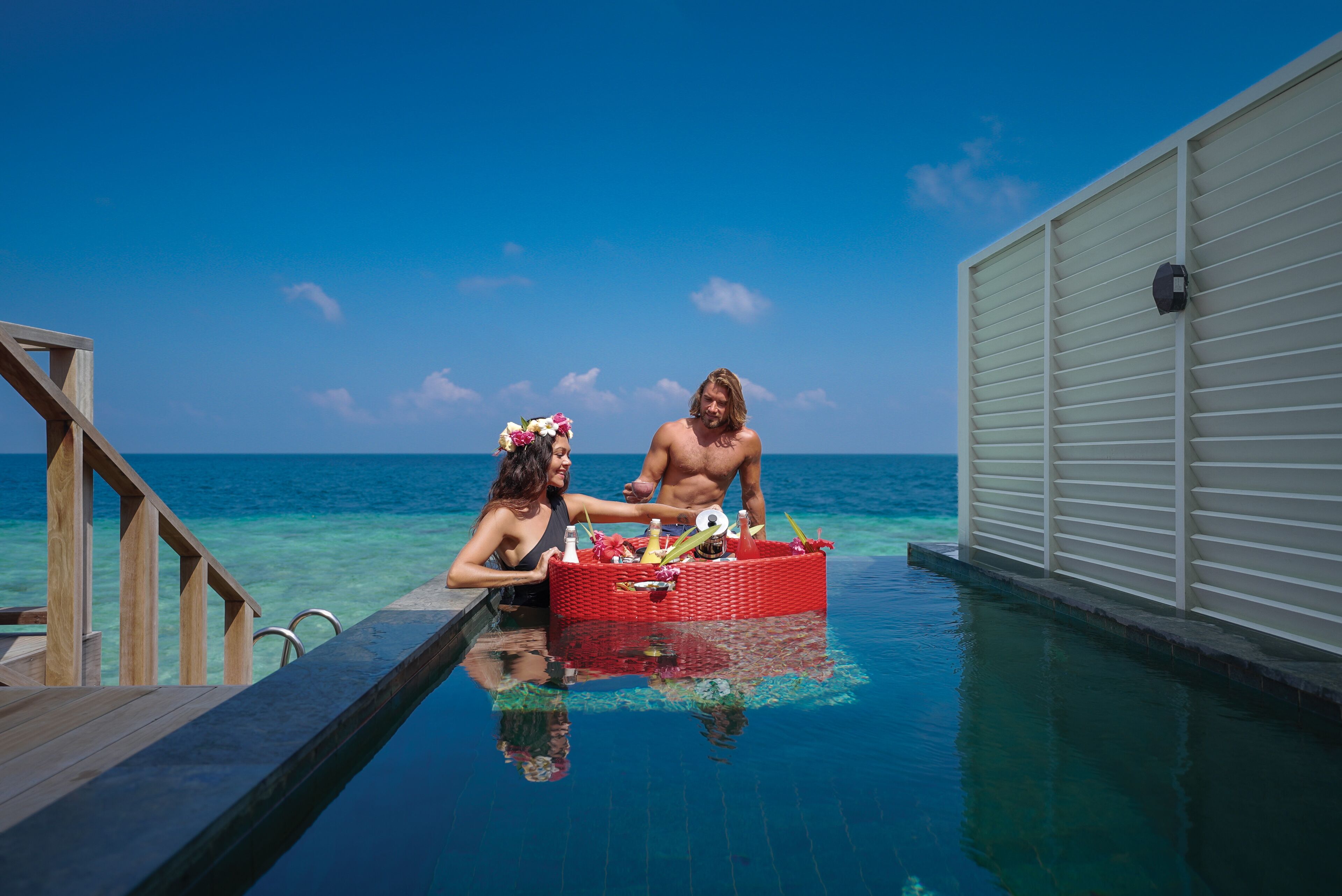 A couple in a pool with a wooden deck and a white building in the background.