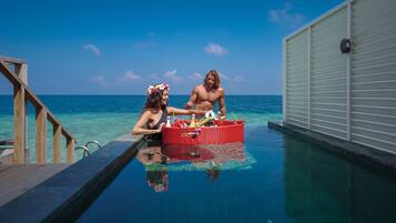 A couple in a pool with a wooden deck and a white building in the background.