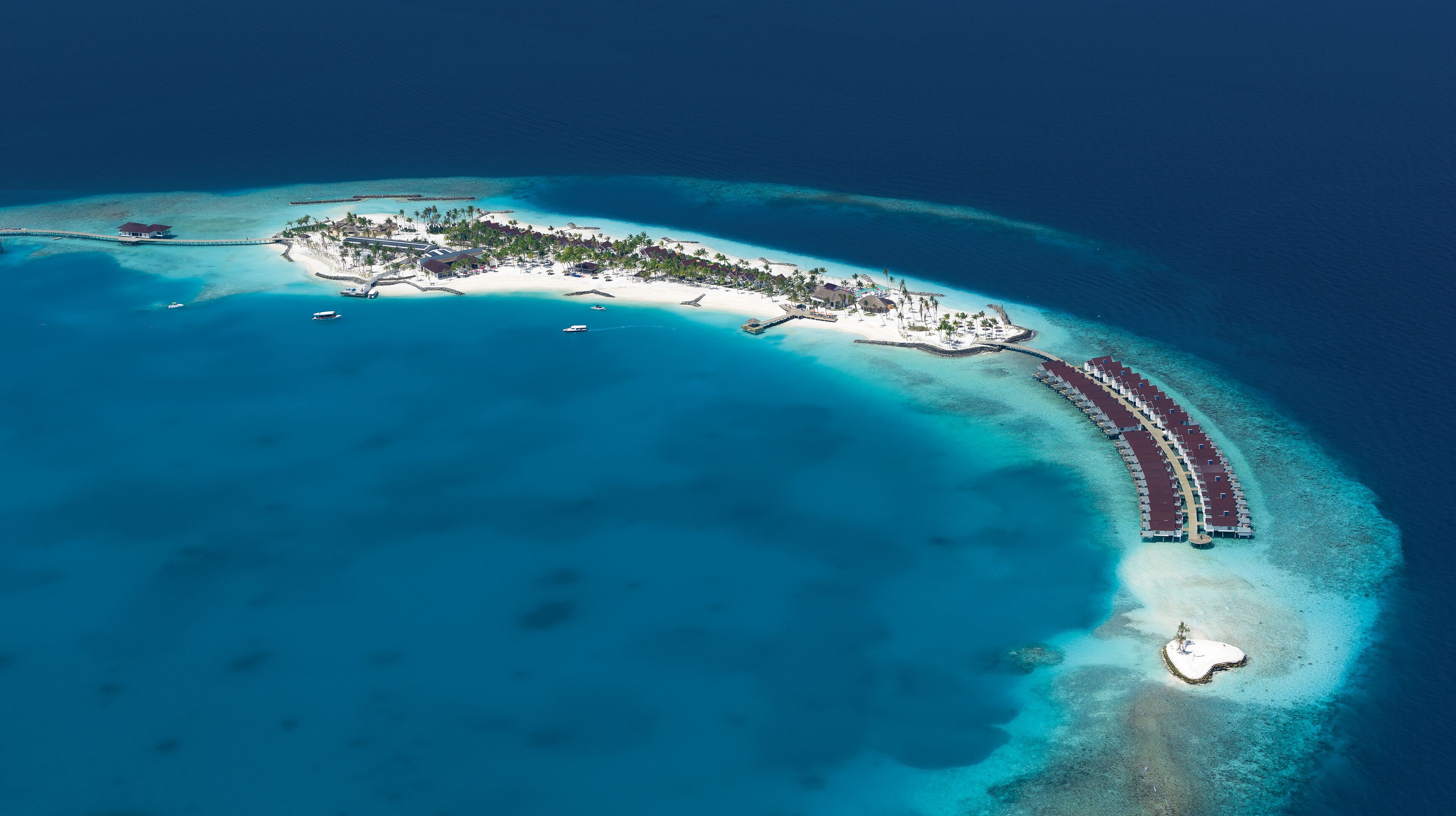 An aerial view of a resort island with a long pier, white sandy beaches, and clear blue waters.