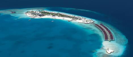 An aerial view of a resort island with a long pier, white sandy beaches, and clear blue waters.