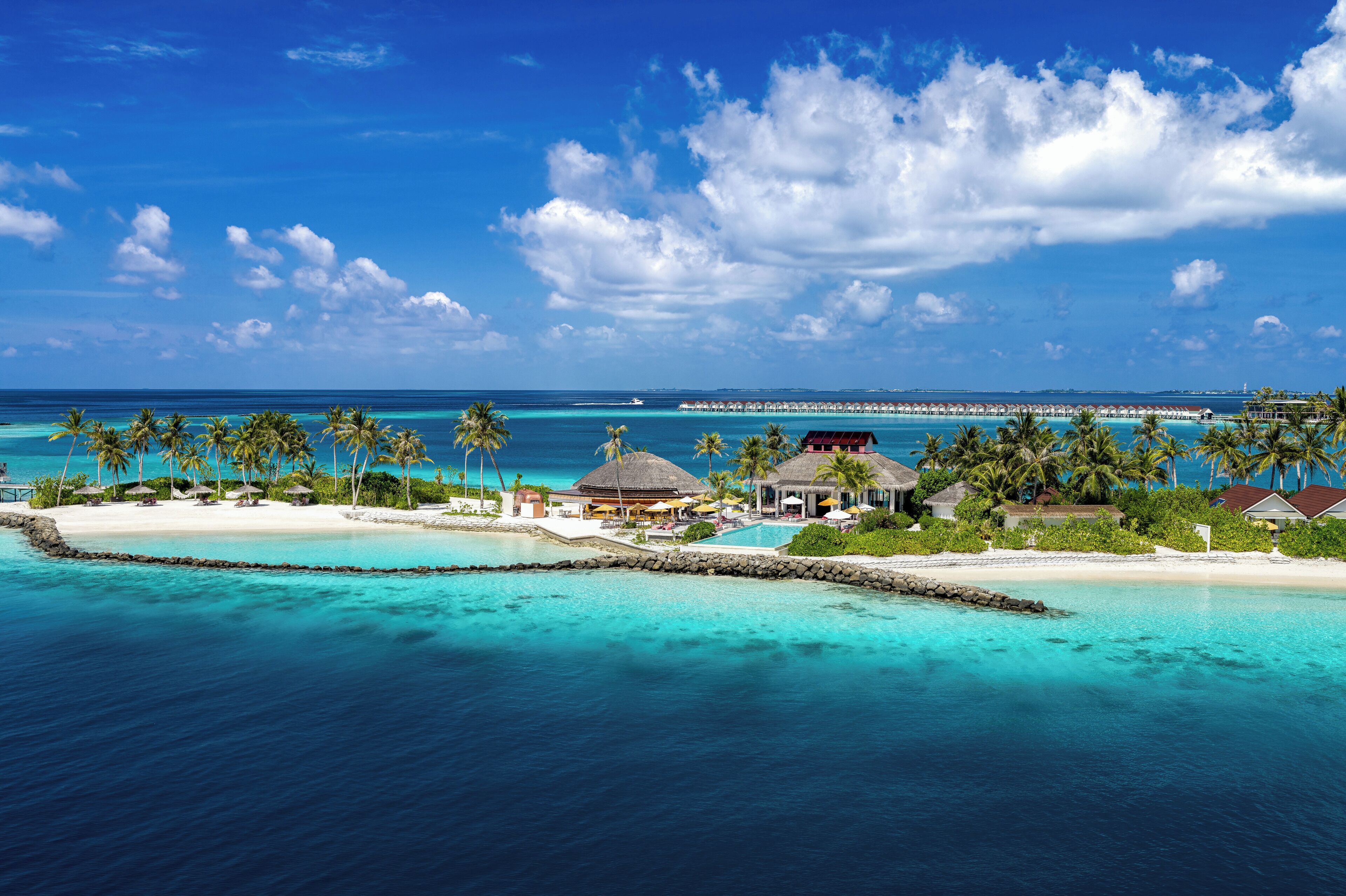 Un resort tropical con bungalows sobre el agua, una piscina y una playa.