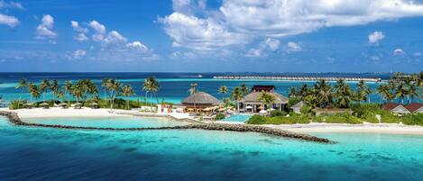 Un resort tropical con bungalows sobre el agua, una piscina y una playa.