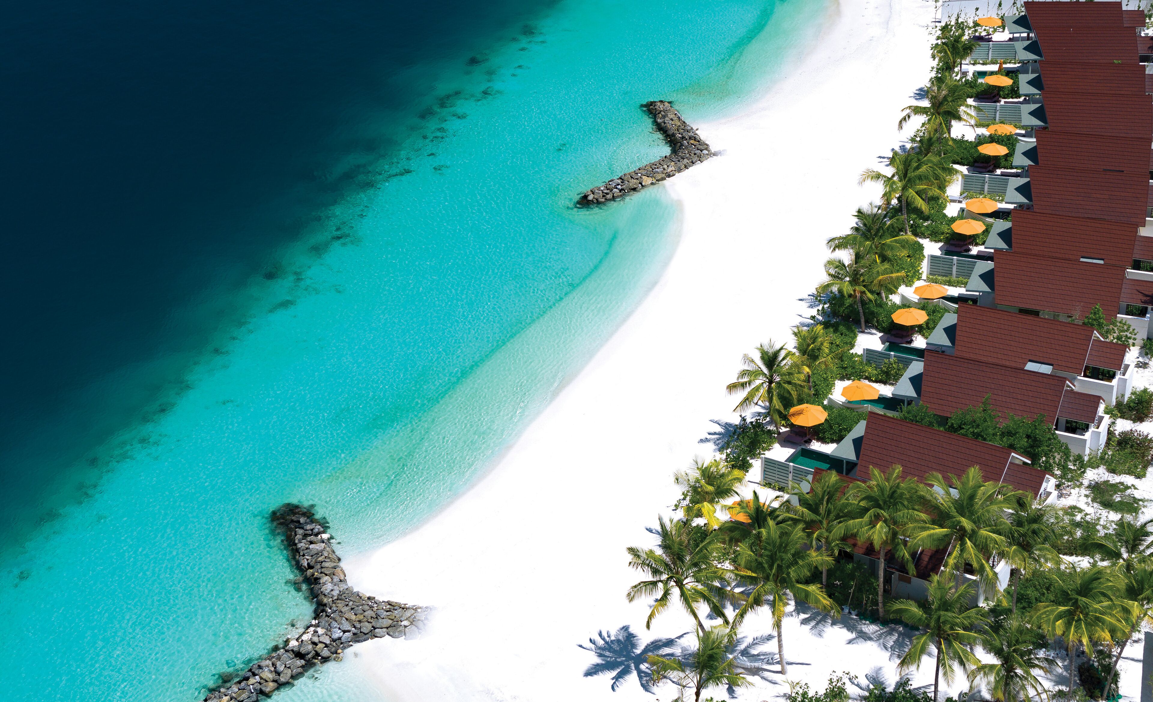 Un resort con playa, un rompeolas rocoso y filas de habitaciones con sombrillas.