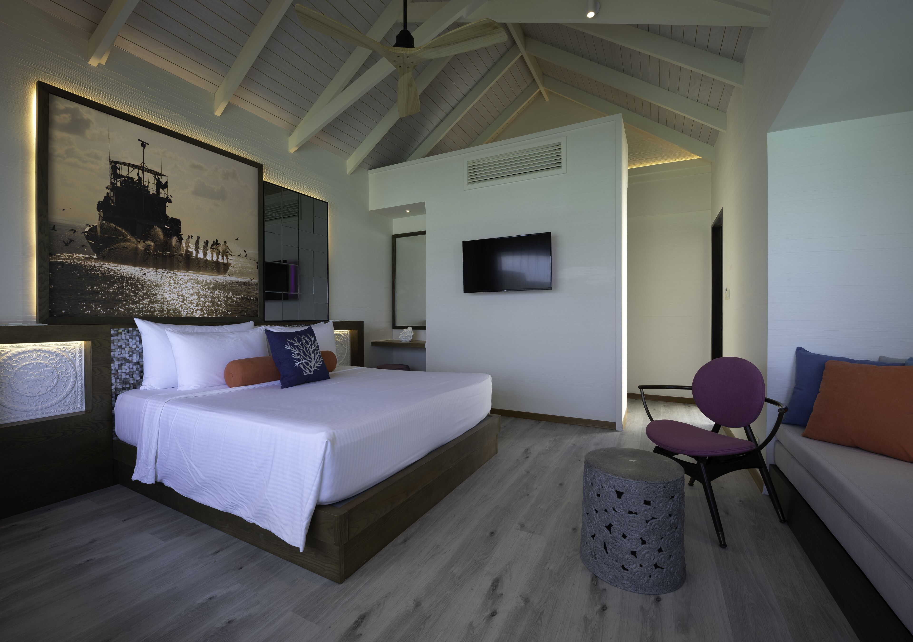 A modern bedroom with a large bed, a television, and a seating area with a chair and sofa.