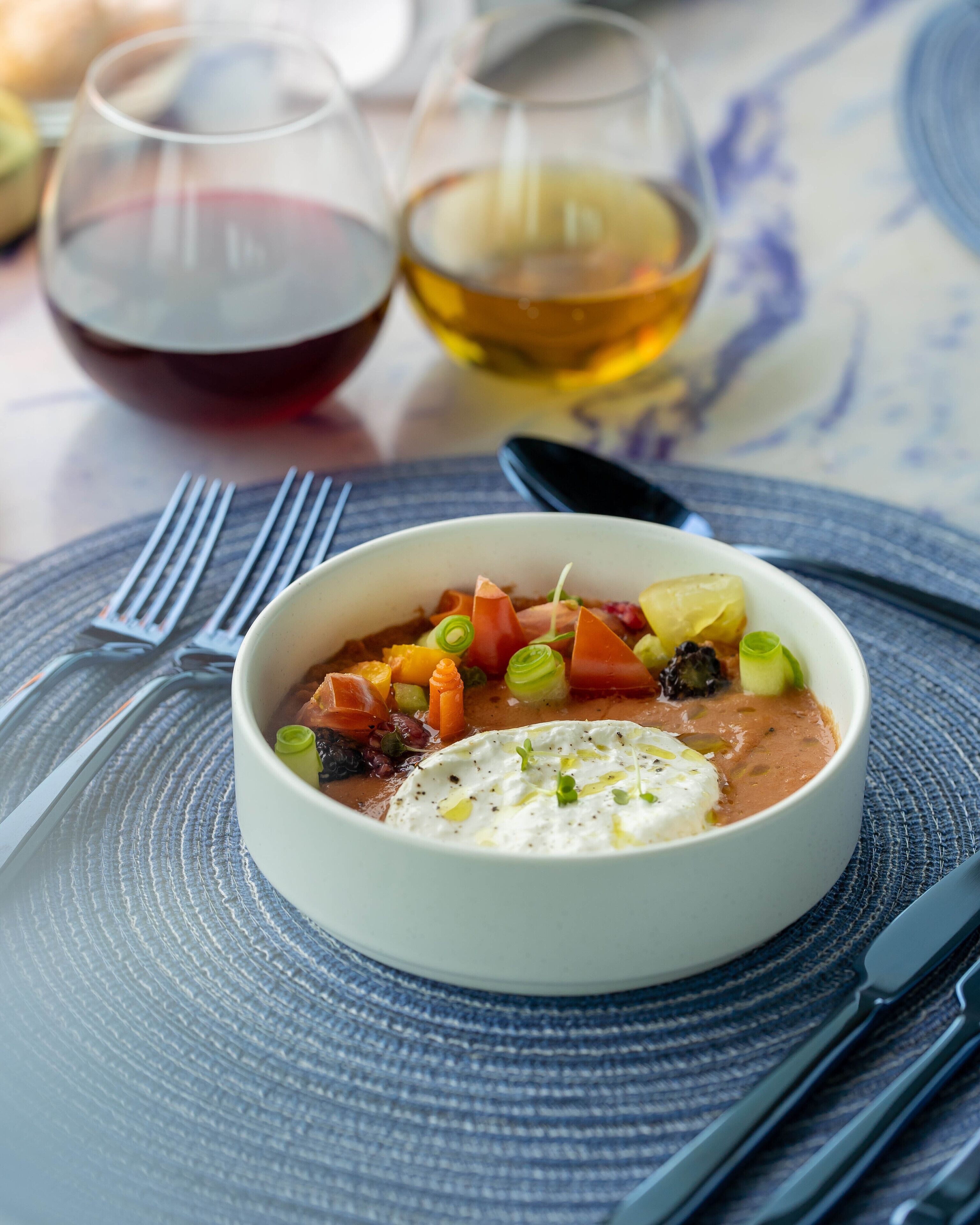 A bowl of soup with vegetables and a dollop of cream on a textured placemat.