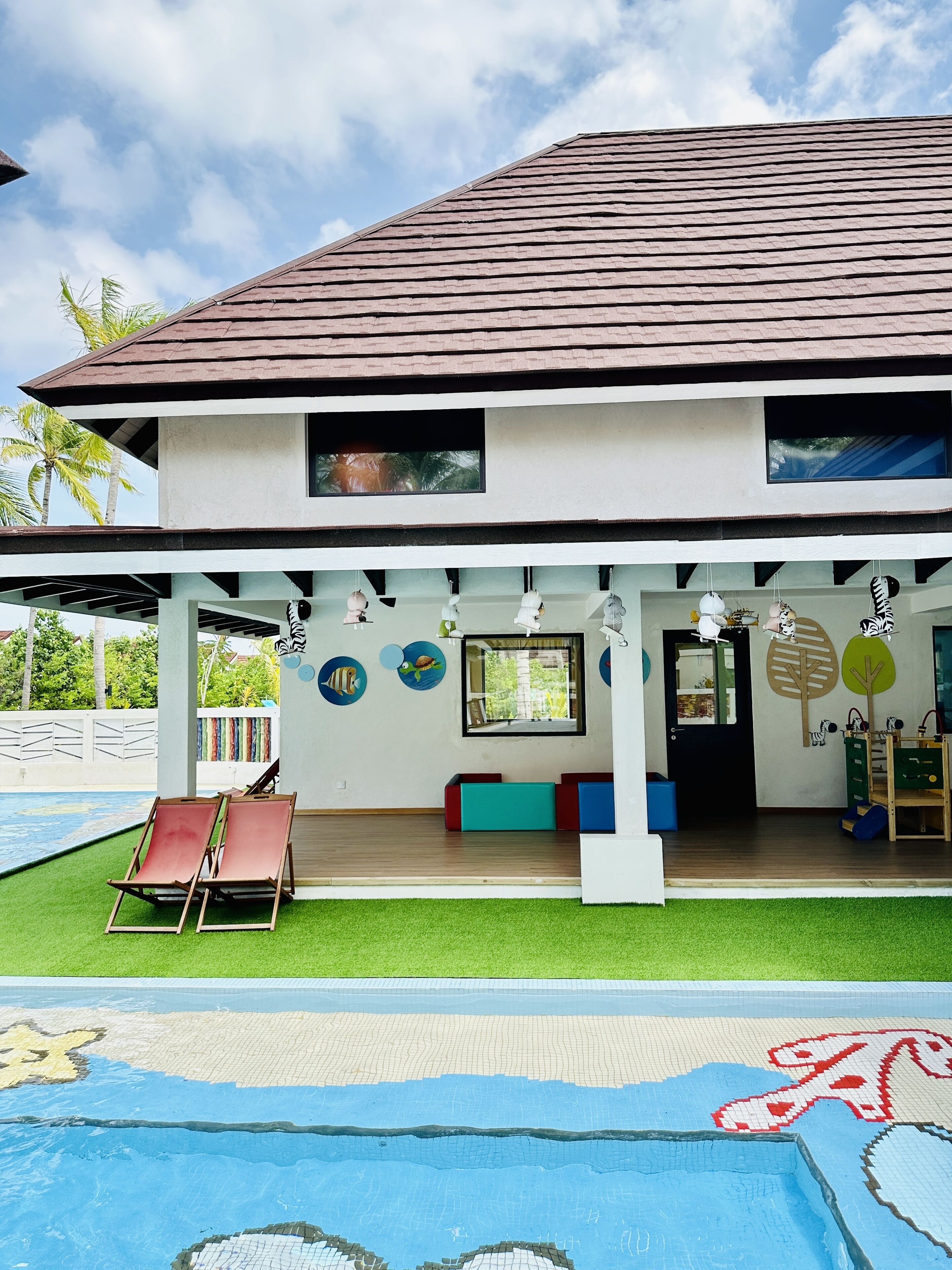 Un edificio de dos pisos con piscina, un patio cubierto y una zona de juegos infantiles.