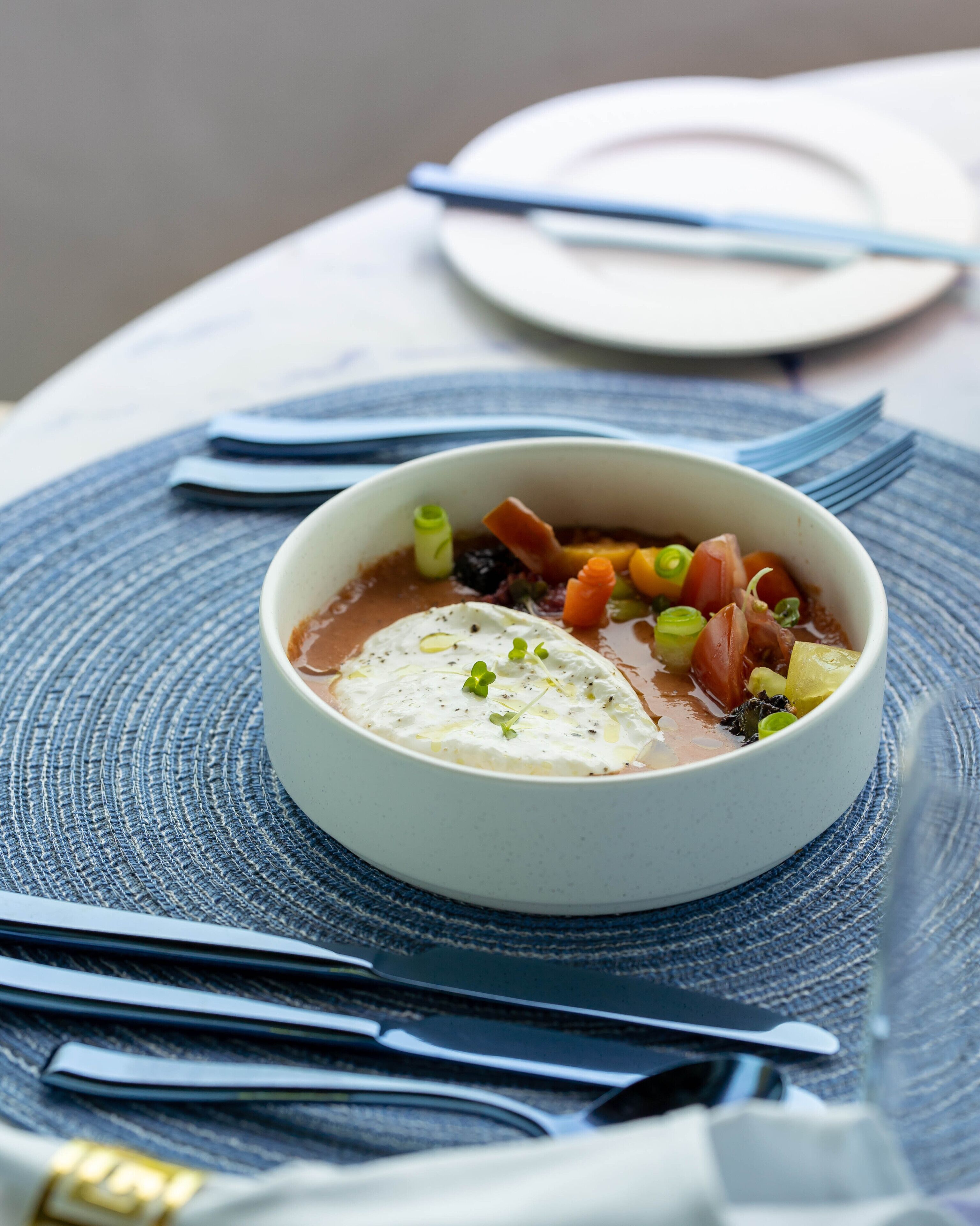 A bowl of soup with vegetables and a dollop of cream on a textured placemat.