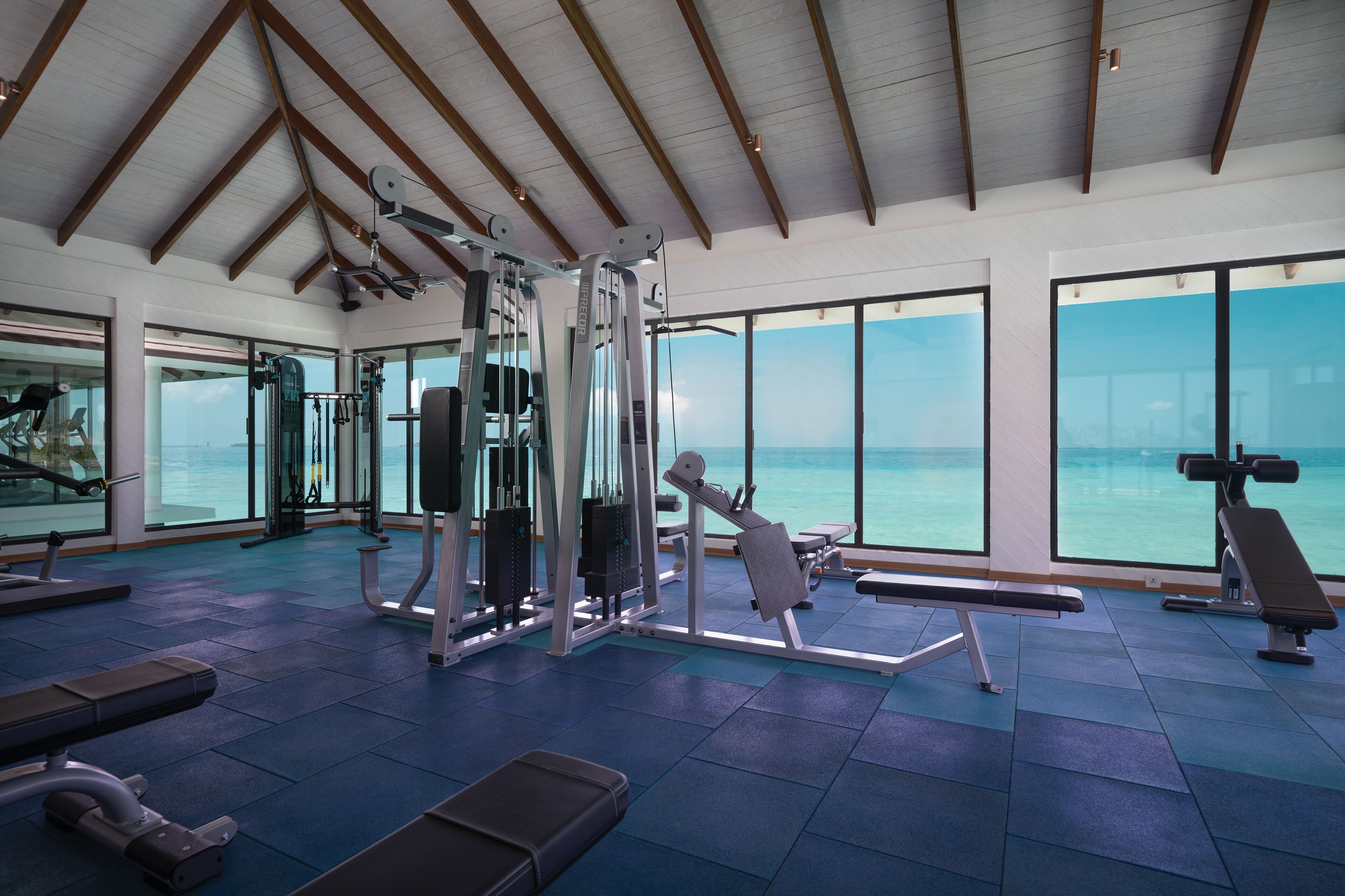 Ein Fitnessraum mit Trainingsgeräten und großen Fenstern mit Meerblick.