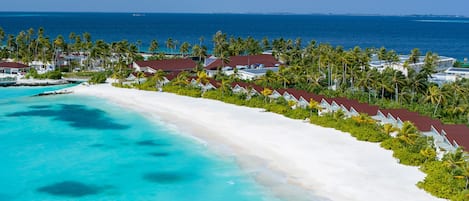 Resort com praia, palmeiras e vista para o oceano.