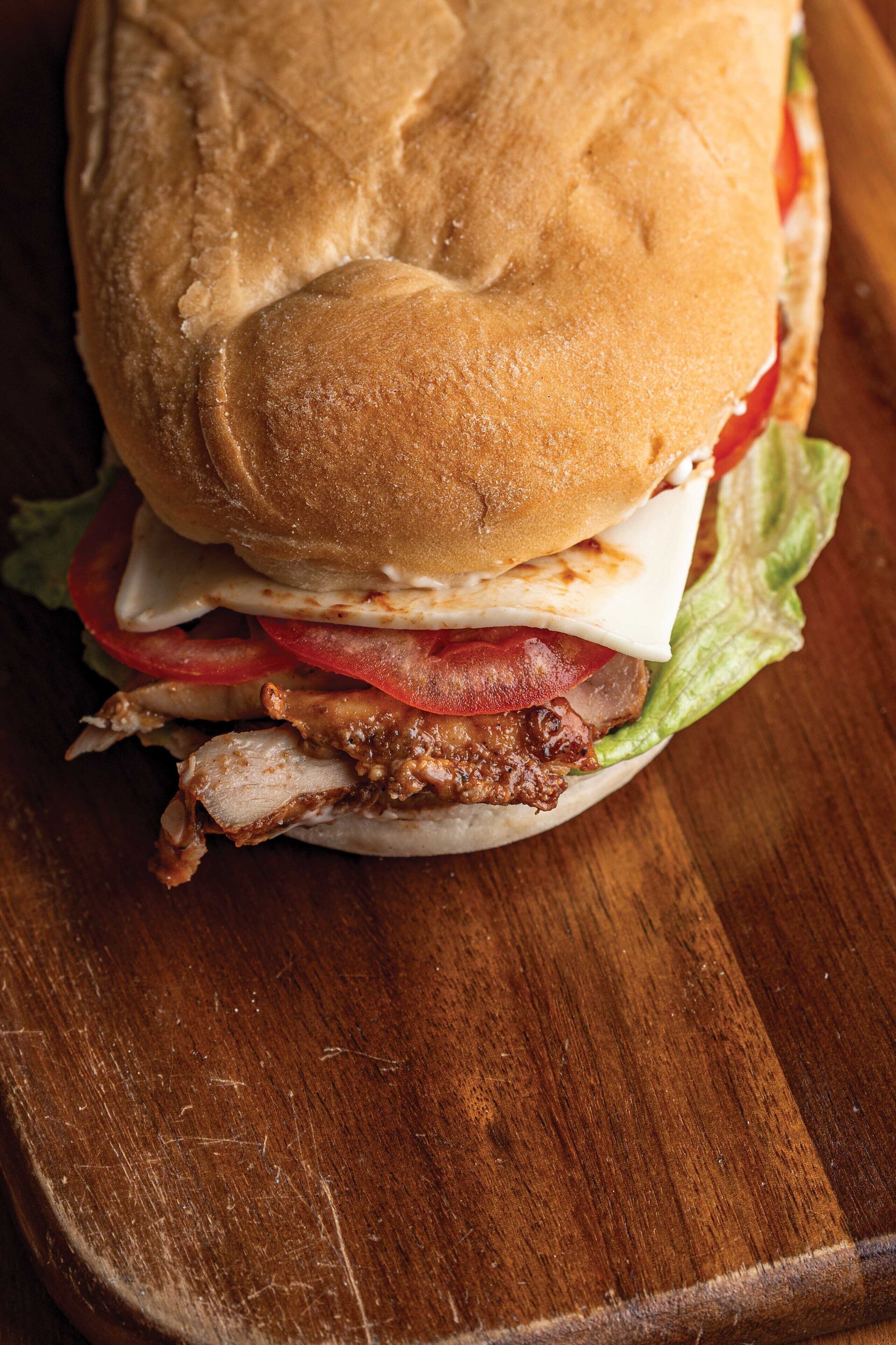Un sándwich con lechuga, tomate, queso y carne sobre una superficie de madera.