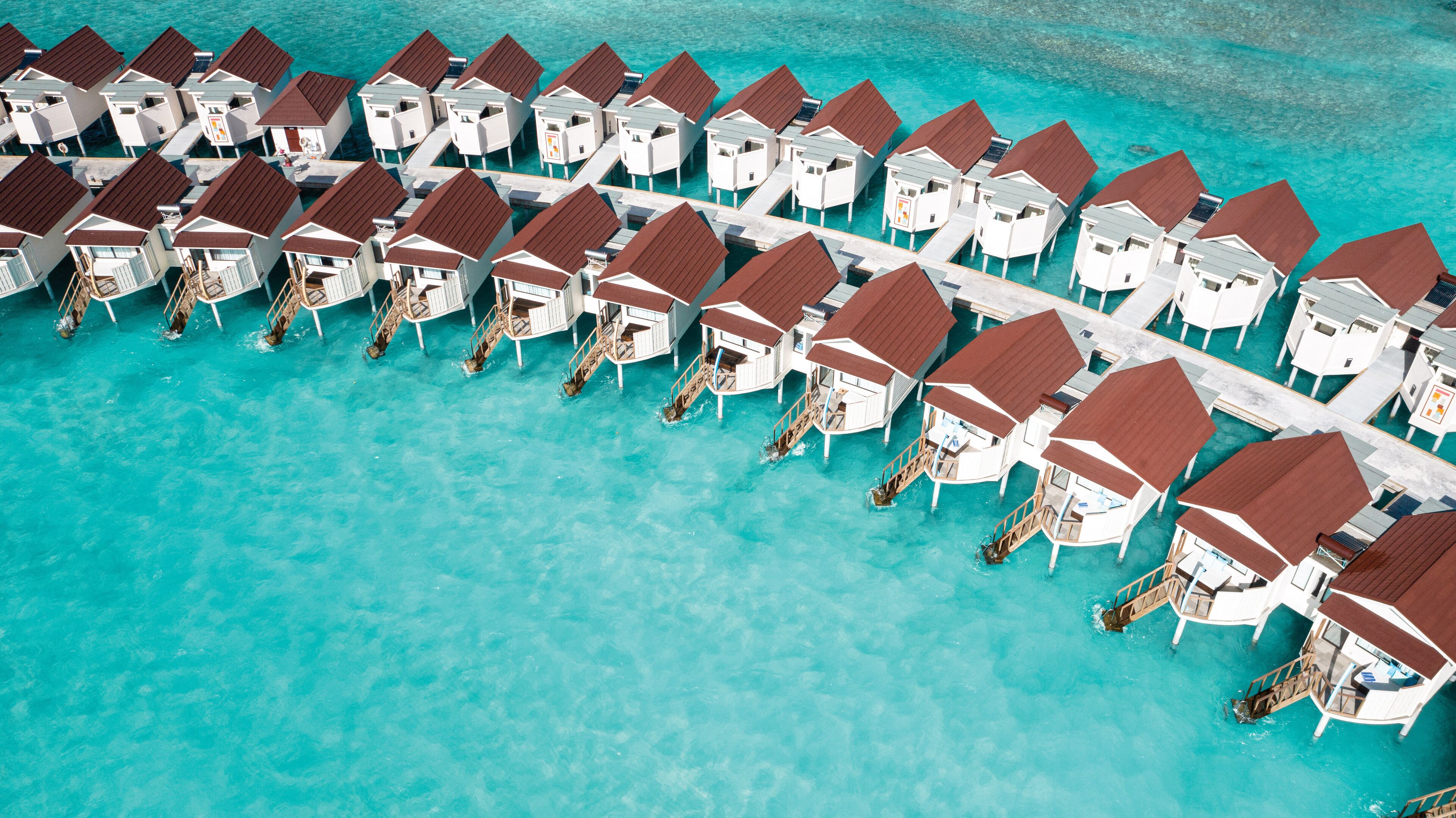 An aerial view of overwater bungalows arranged in rows with clear turquoise water.