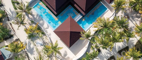Vista aérea de un resort con una piscina central rodeada de palmeras y un diseño geométrico para la zona de la piscina.