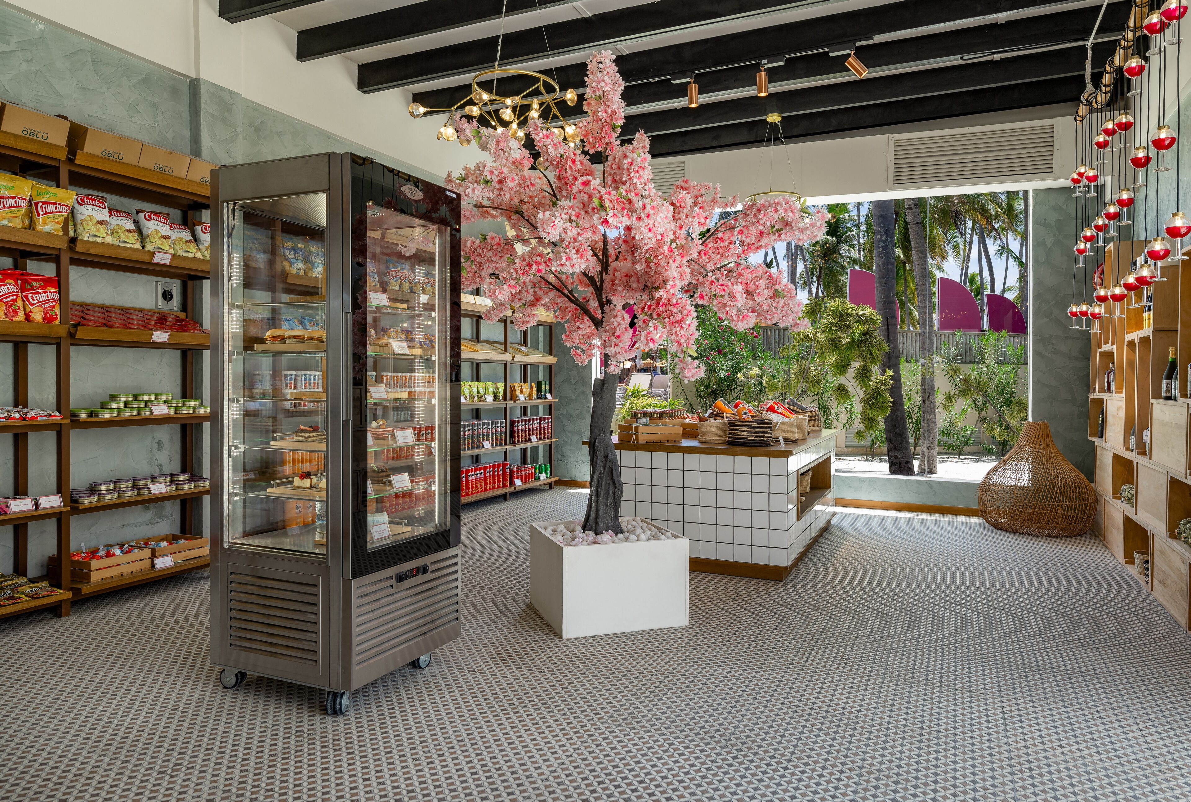 A modern interior with a refrigerated display, a central tree, and shelves stocked with snacks.