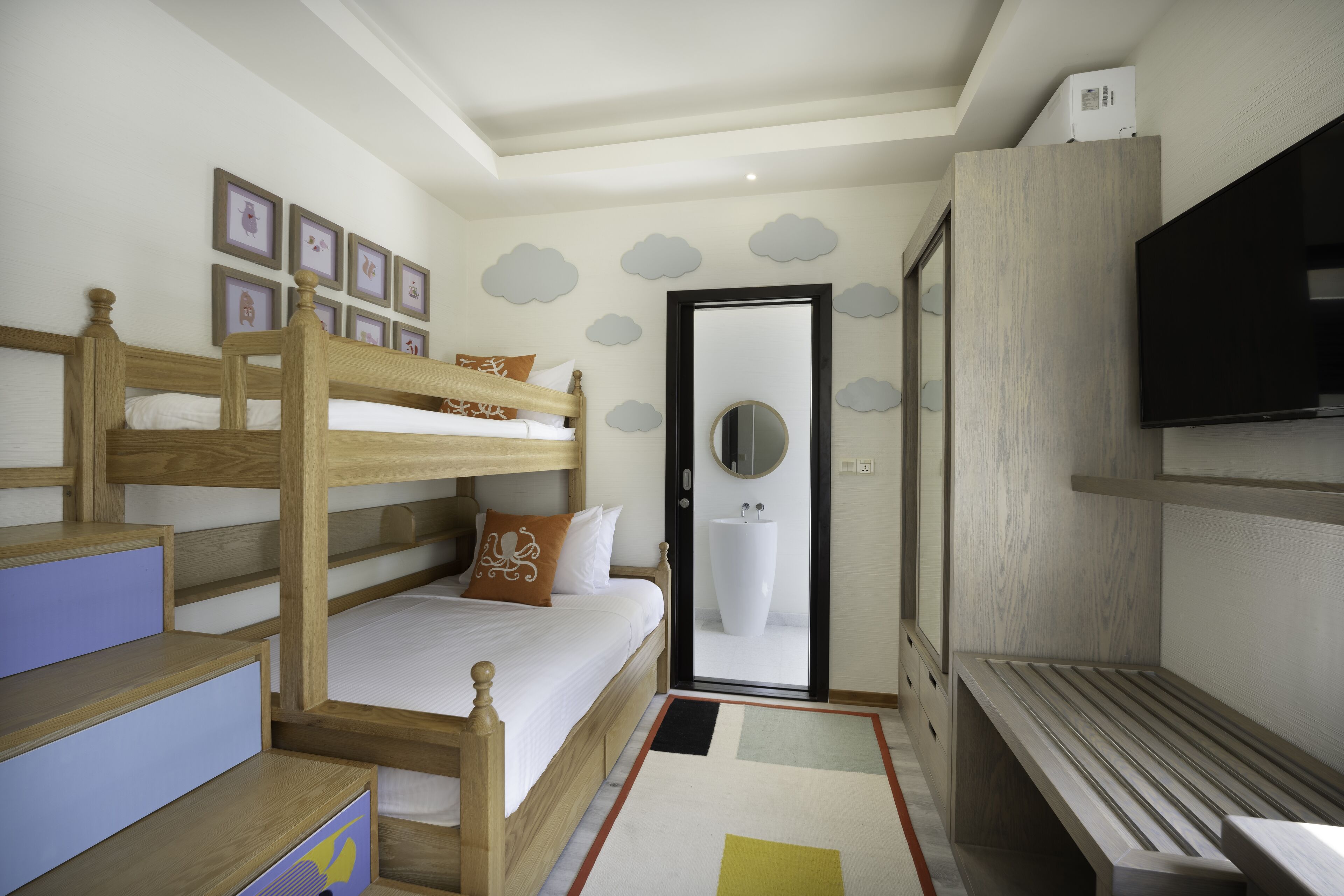 A bedroom with bunk beds, a TV, a bathroom with a large mirror, and cloud-themed wall decorations.