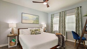 A bedroom with a bed, two bedside tables, a ceiling fan, a window with curtains, and a chair.