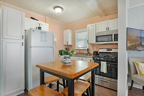Cocina compacta con armarios blancos, un refrigerador, un microondas, un horno y una mesa con bancos.
