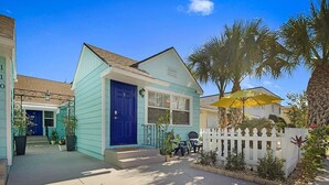 A house with a blue door, a white picket fence, and a yellow umbrella.