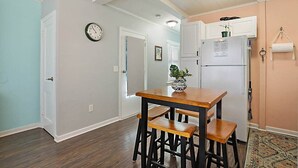 A kitchen with a wooden table and chairs, a clock on the wall, and a refrigerator with a note.