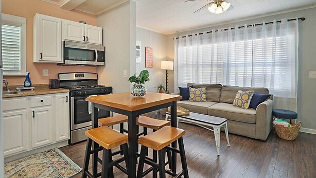 A kitchen with white cabinets, a microwave, stove, and a dining area with a table and bar stools.
