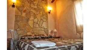 Une chambre avec un mur en pierre, un lit recouvert d’une couvre-lit à motifs, deux lampes fixées au mur et une table de chevet avec une lampe.