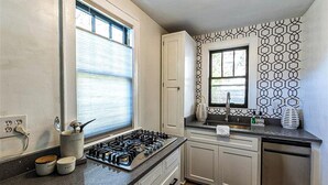 A kitchen with a gas stove, cabinets, a window with blinds, and a patterned backsplash. - Charming, modern, 2nd floor home-away-from-home (Augusta)