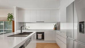 A modern kitchen with white cabinetry, stainless steel appliances, and a wooden floor.