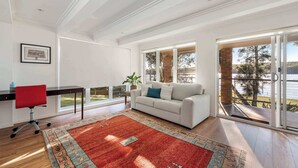 A spacious living room with a large window, a red office chair, a white sofa, and a patterned rug.