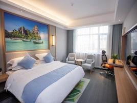 Una habitación de hotel con una cama grande, dos sillones, un escritorio y un ventanal amplio.